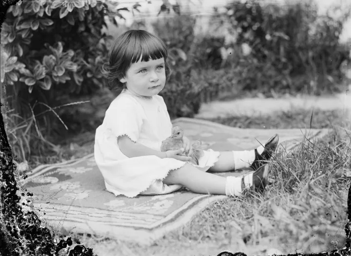 Portrait of a toddler girl seated on a patterned rug on the grass (AM 76336-1)