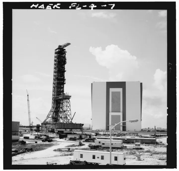 LAUNCHER SIDES 1 AND 2. BUILDING IN BACKGROUND IS VEHICLE ASSEMBLY BUILDING (VAB) WHERE ROCKET WAS ASSEMBLED ON LAUNCHER. - Mobile Launcher One, Kennedy Space C