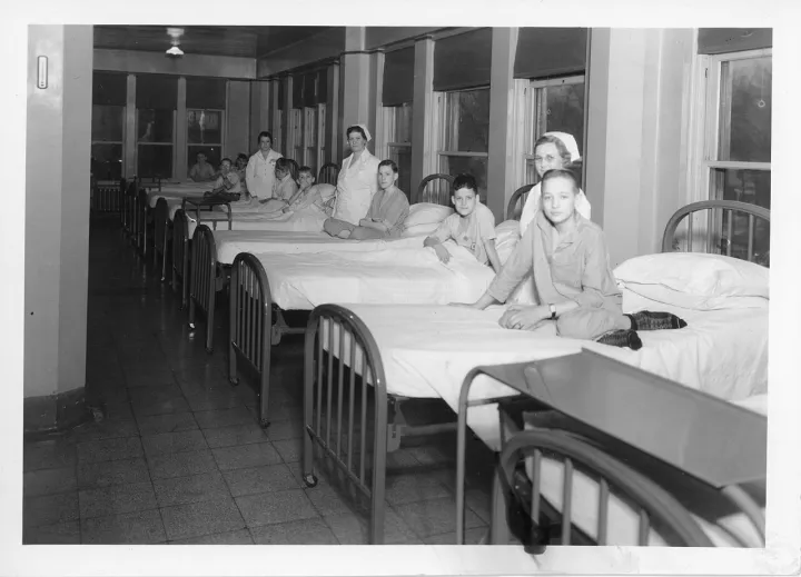 Young patients in beds with nurses standing by